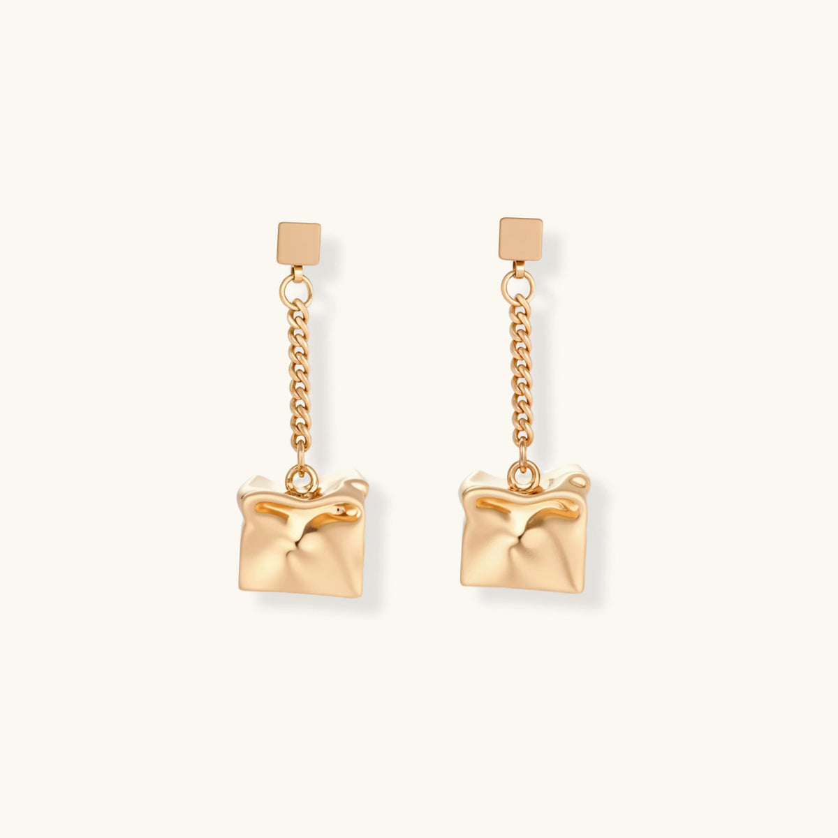 Gold-toned geometric cube earrings with crumpled texture hanging from delicate chains, shown against neutral background.