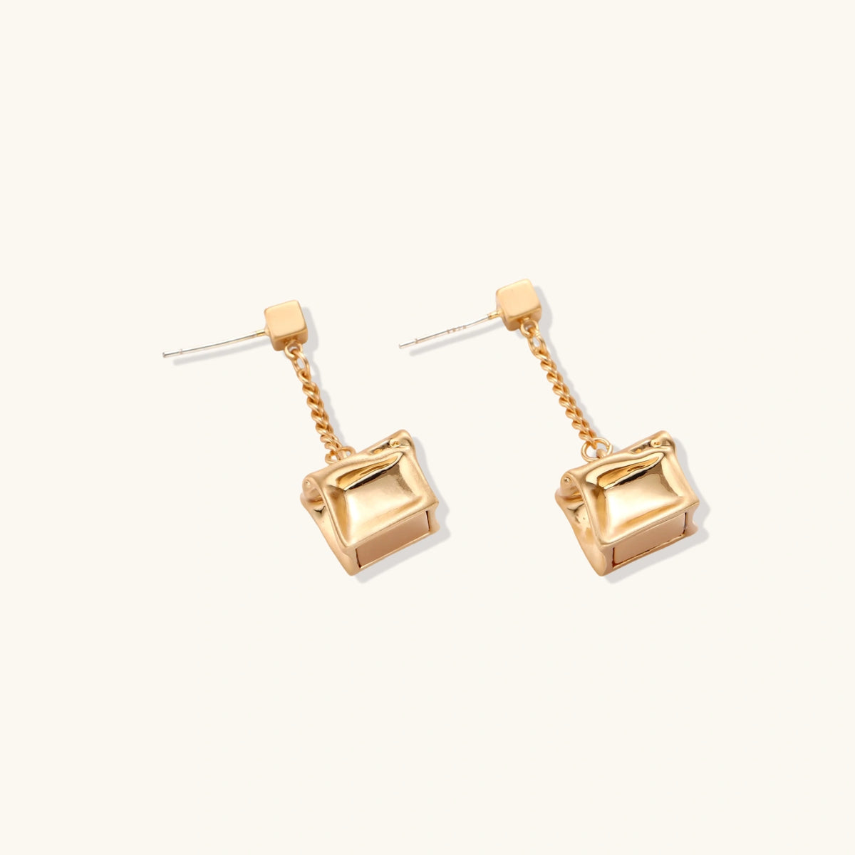 Gold-toned geometric cube earrings with crumpled texture hanging from delicate chains, shown against neutral background.