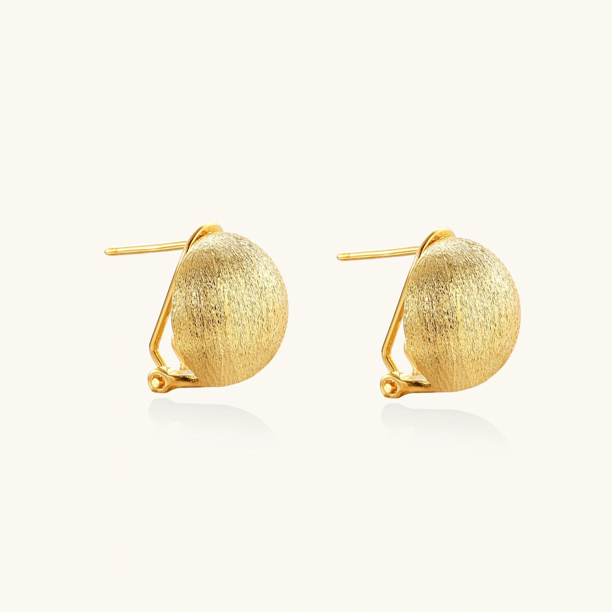 Pair of brushed gold dome earrings with clip backs showing textured matte finish on cream background