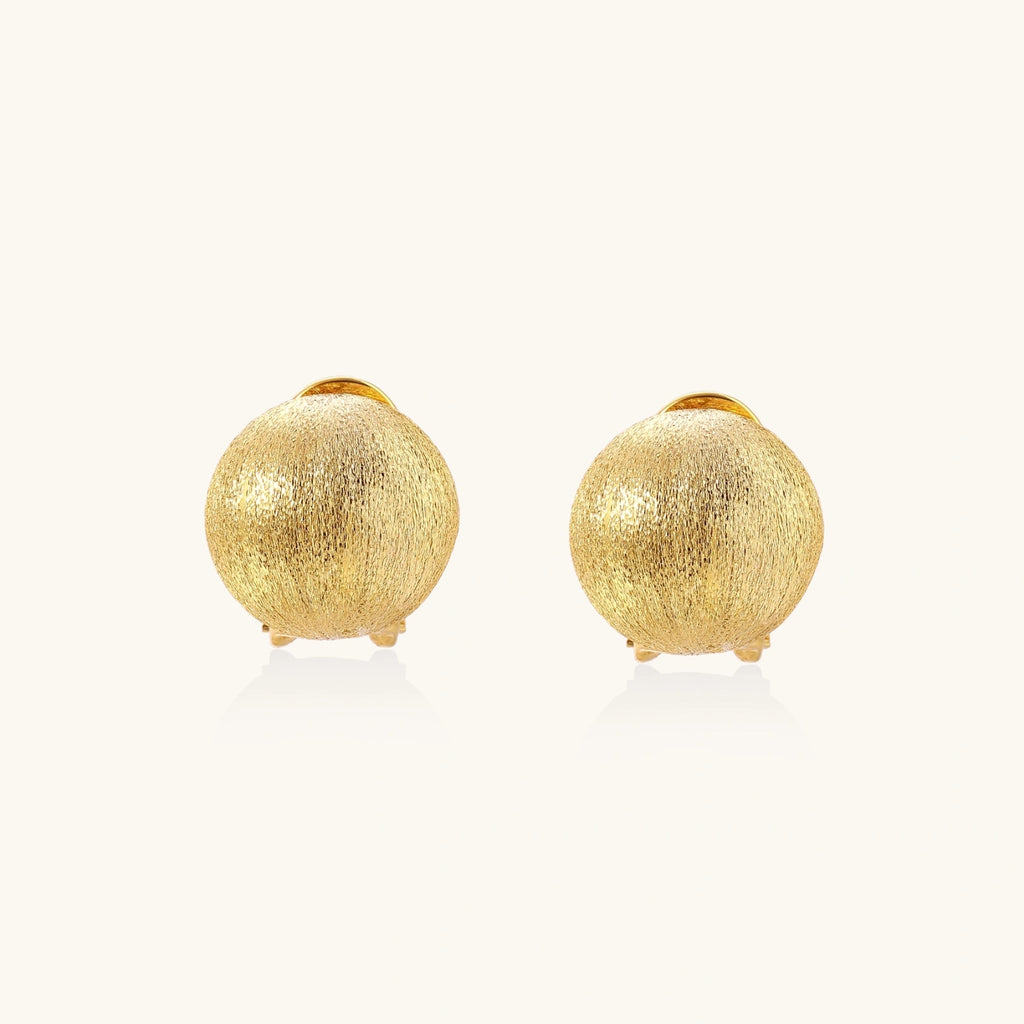 Pair of brushed gold dome earrings with clip backs showing textured matte finish on cream background