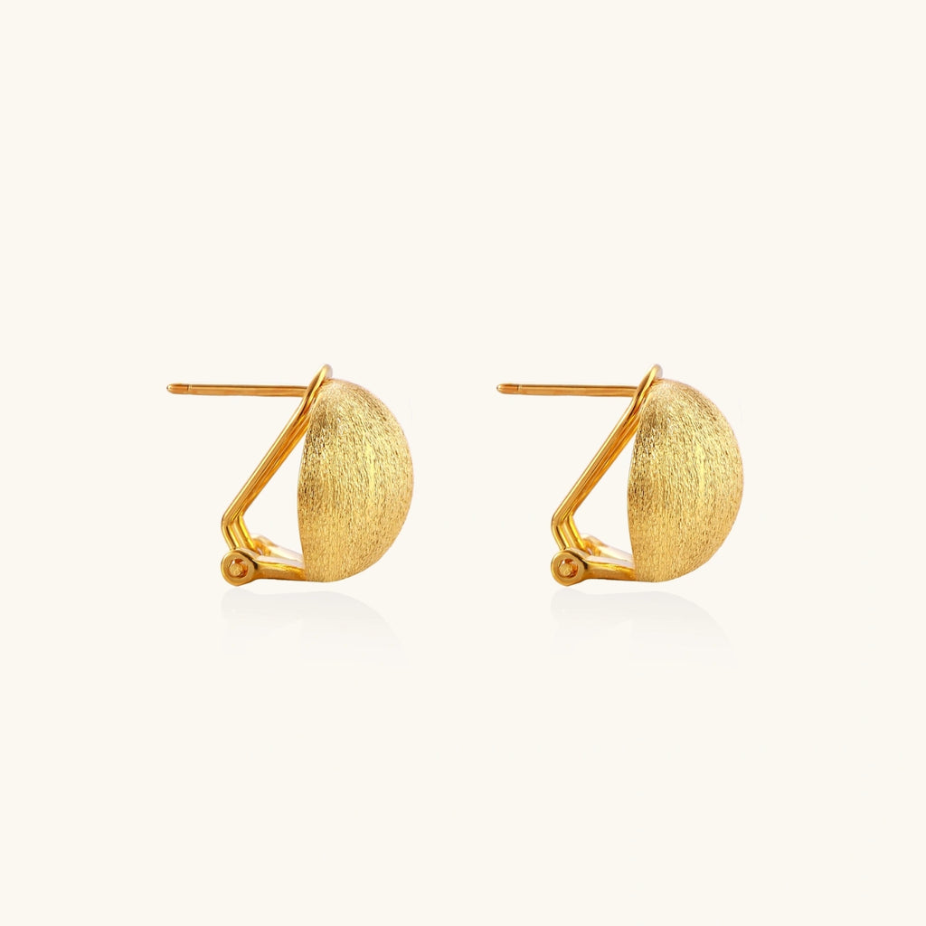 Pair of brushed gold dome earrings with clip backs showing textured matte finish on cream background